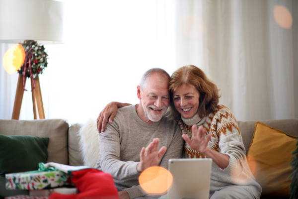 Happy senior couple indoors at home at Christmas, having video call with family.