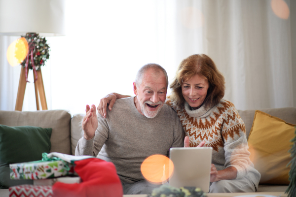 Front view of happy senior couple indoors at home at Christmas, having video call with family.