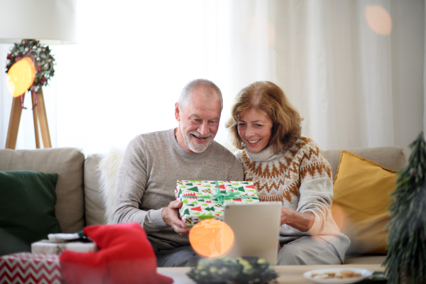 Front view of happy senior couple indoors at home at Christmas, having video call with family.