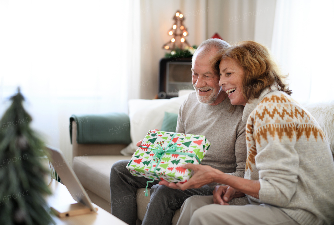 Side view of happy senior couple indoors at home at Christmas, having video call with family.