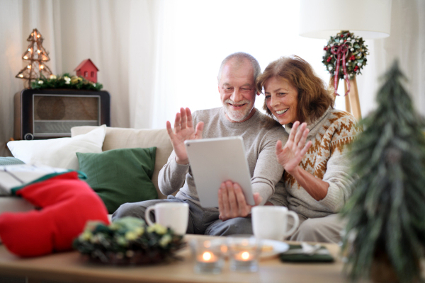 Front view of happy senior couple indoors at home at Christmas, having video call with family.