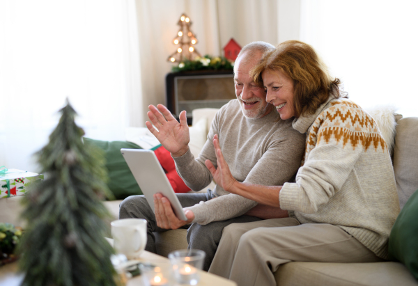 Side view of happy senior couple indoors at home at Christmas, having video call with family.