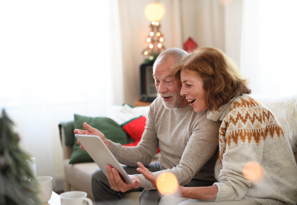 Side view of happy senior couple indoors at home at Christmas, having video call with family.