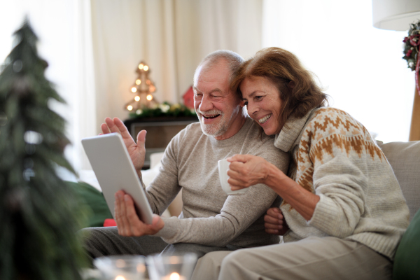 Side view of happy senior couple indoors at home at Christmas, having video call with family.