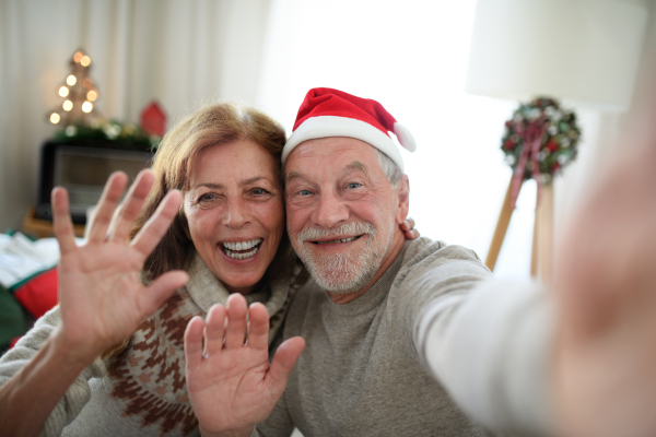 Front view of happy senior couple indoors at home at Christmas, taking selfie.