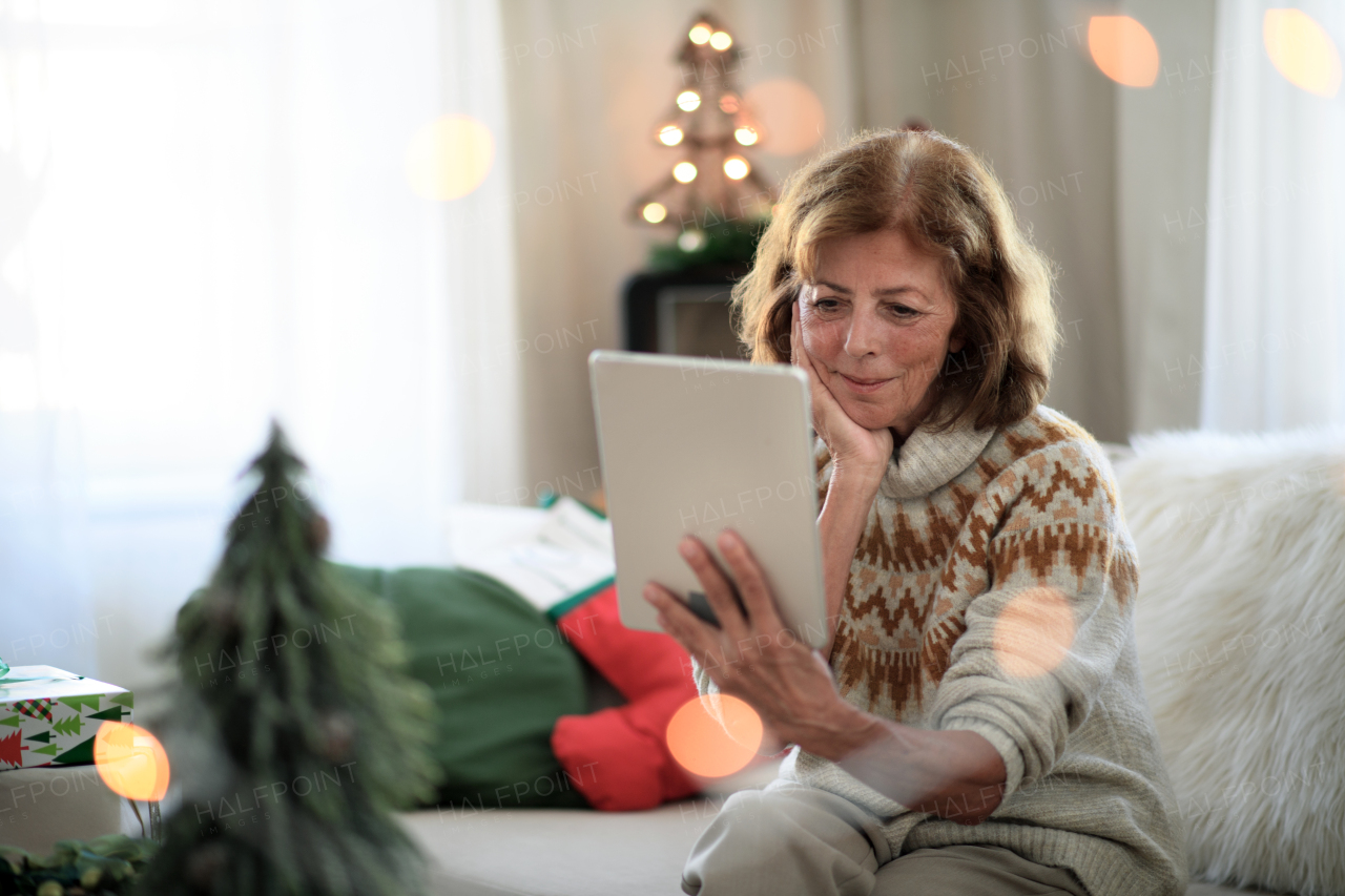 Portrait of senior woman indoors at home at Christmas, having video call with family.