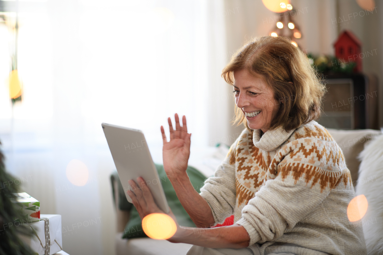 Side view of happy senior woman indoors at home at Christmas, having video call with family.