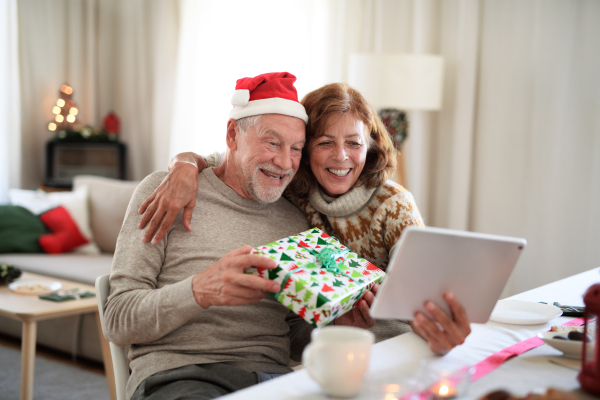 Front view of happy senior couple indoors at home at Christmas, having video call with family.