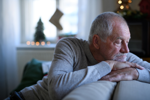 Portrait of lonely senior man sitting and sleeping on sofa indoors at Christmas, solitude concept.