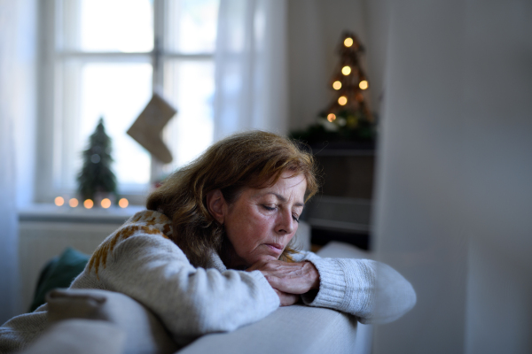 Portrait of lonely senior woman sitting and sleeping on sofa indoors at Christmas, solitude concept.