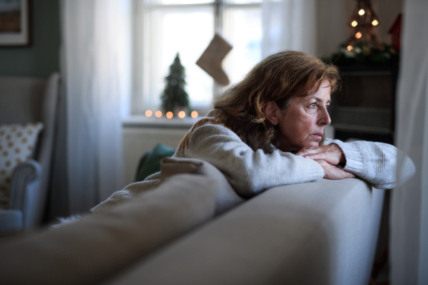 Portrait of lonely senior woman sitting on sofa indoors at Christmas, solitude concept.