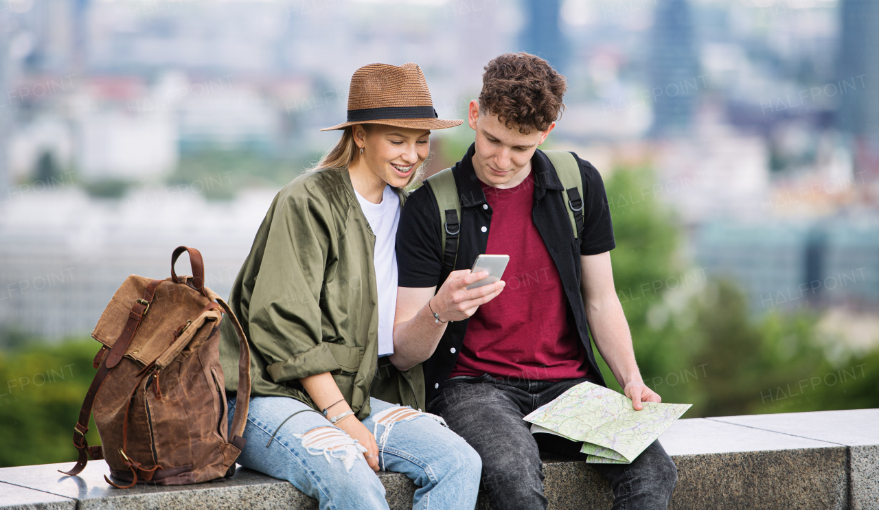 Portrait of young couple travelers with map in city on holiday, using smartphone.