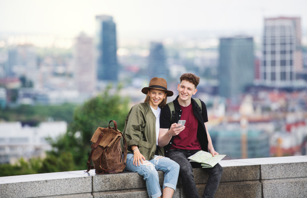 A young couple travelers with map in city on holiday, using smartphone.