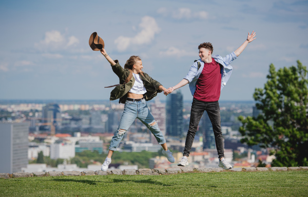 A cheerful young couple travelers in city on holiday, jumping. Cityscape in the background.