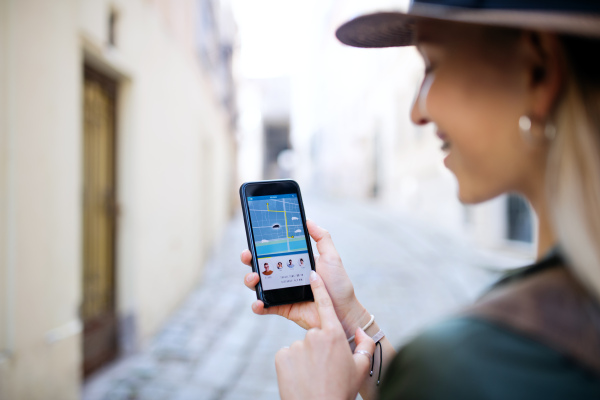 Unrecognizable young woman traveler with smartphone in city on holiday, car sharing concept.