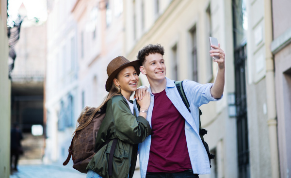 A young couple travelers with smartphone sightseeing in city on holiday, taking selfie.