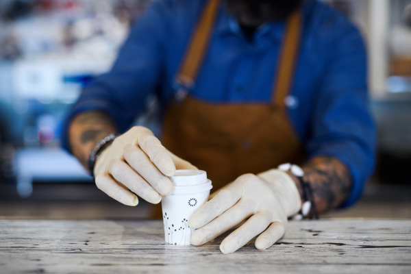 Unrecognizable barista working with gloves, coffee shop open after lockdown quarantine.