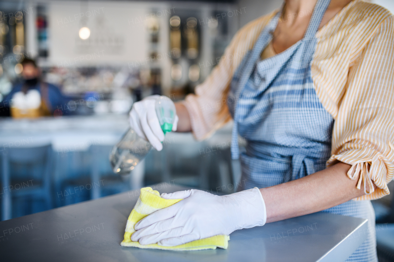 Midsection of unrecognizable woman working with gloves in coffee shop, disinfecting tables.