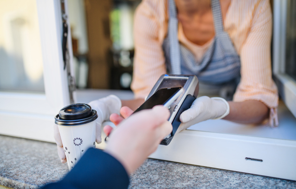 Woman serving coffee through window after quarantine, contactless payment and back to normal concept.