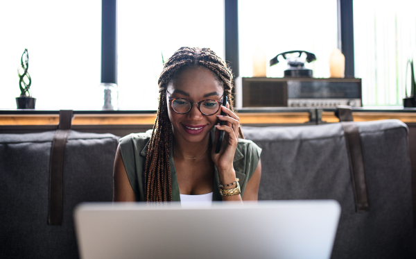 Portrait of young business woman with laptop and smartphone working indoors in office.