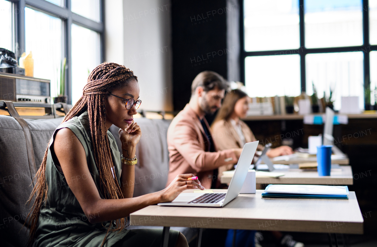 Portrait of young businesspeople with laptop sitting and working indoors in office.