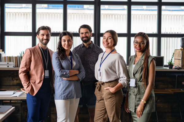 Front view portrait of young businesspeople standing indoors in office, looking at camera.