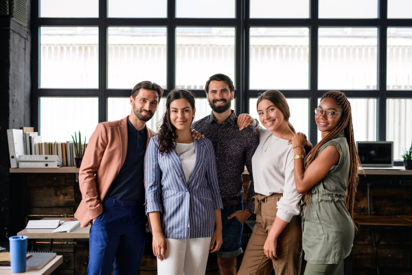 Front view portrait of young businesspeople standing indoors in office, looking at camera.