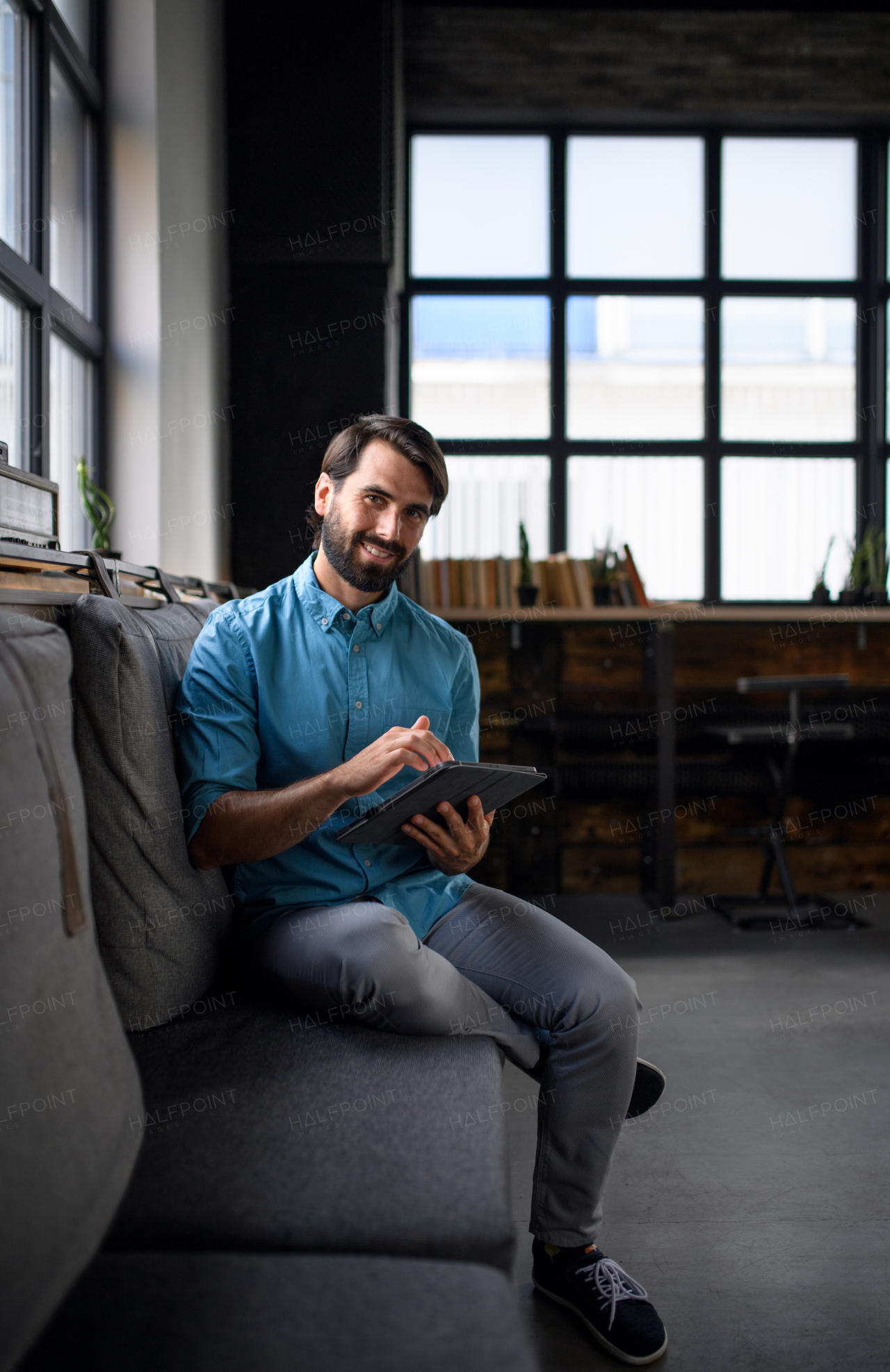 Portrait of young businessman with tablet sitting indoors in office, looking at camera.