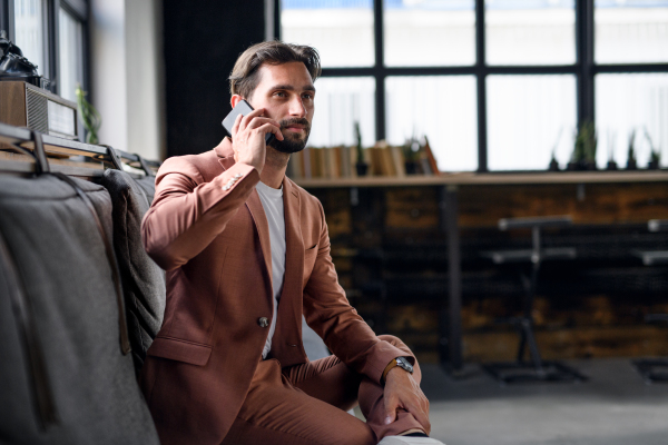 Portrait of young businessman with smartphone sitting indoors in office, looking at camera.