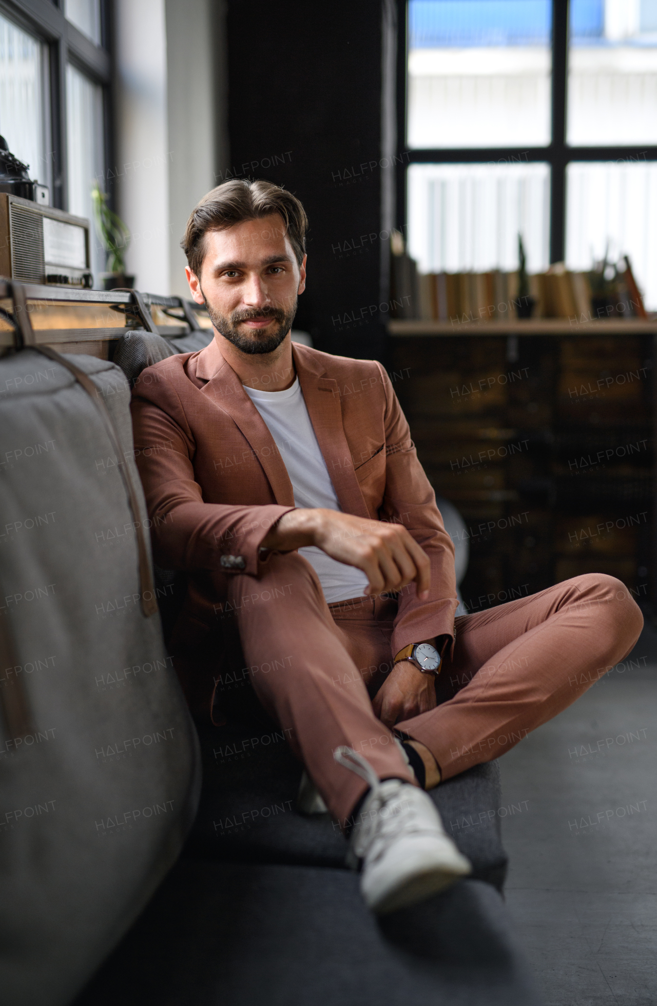 Portrait of young businessman sitting indoors in office, looking at camera.