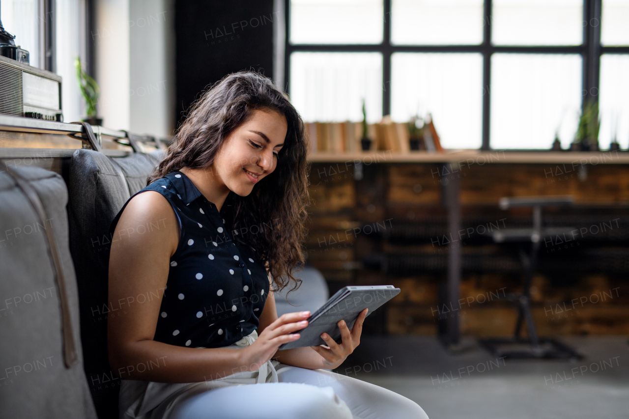 Side view portrait of young businesswoman indoors in office, using tablet.