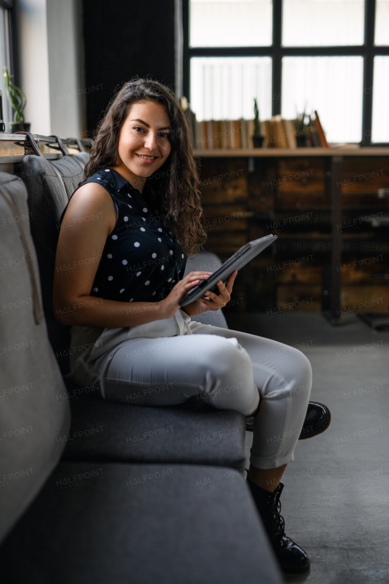 Portrait of young businesswoman sitting indoors in office, looking at camera.