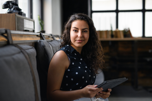 Portrait of young businesswoman sitting indoors in office, looking at camera.