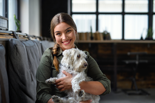 Portrait of young business woman with dog sitting indoors in office, looking at camera.