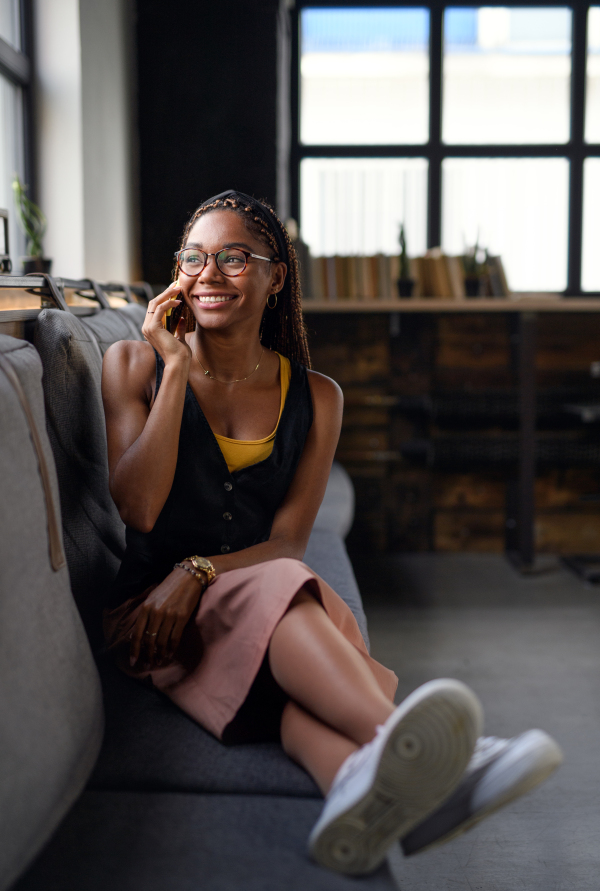 Portrait of young african-american business woman indoors in office, using smartphone.