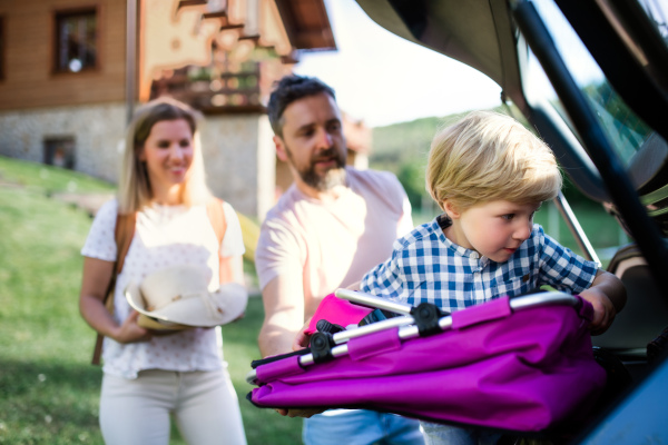 Family with small child going on trip in countryside, putting things in car boot.