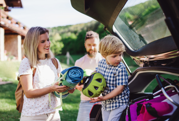 Family with small child going on cycling trip in countryside, putting things in car boot.