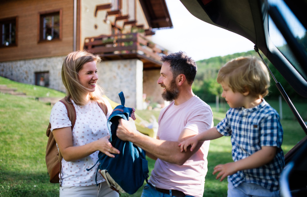 Family with small child going on trip in countryside, putting things in car boot.