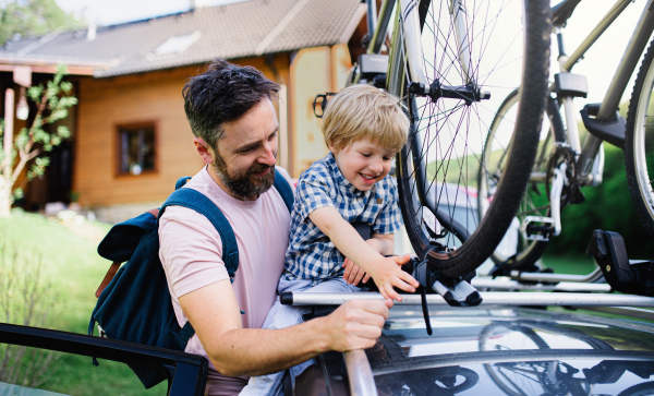 Mature father with small son putting bicycles on car roof, going on trip concept.