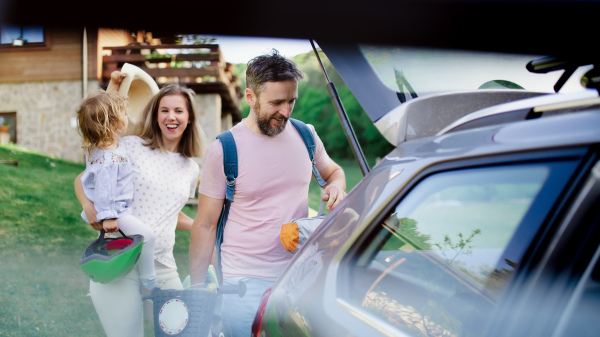 Family with small child going on cycling trip in countryside, putting things in car boot.