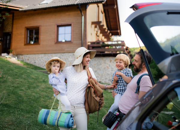 Front view of family with two small children loading car for trip in countryside.