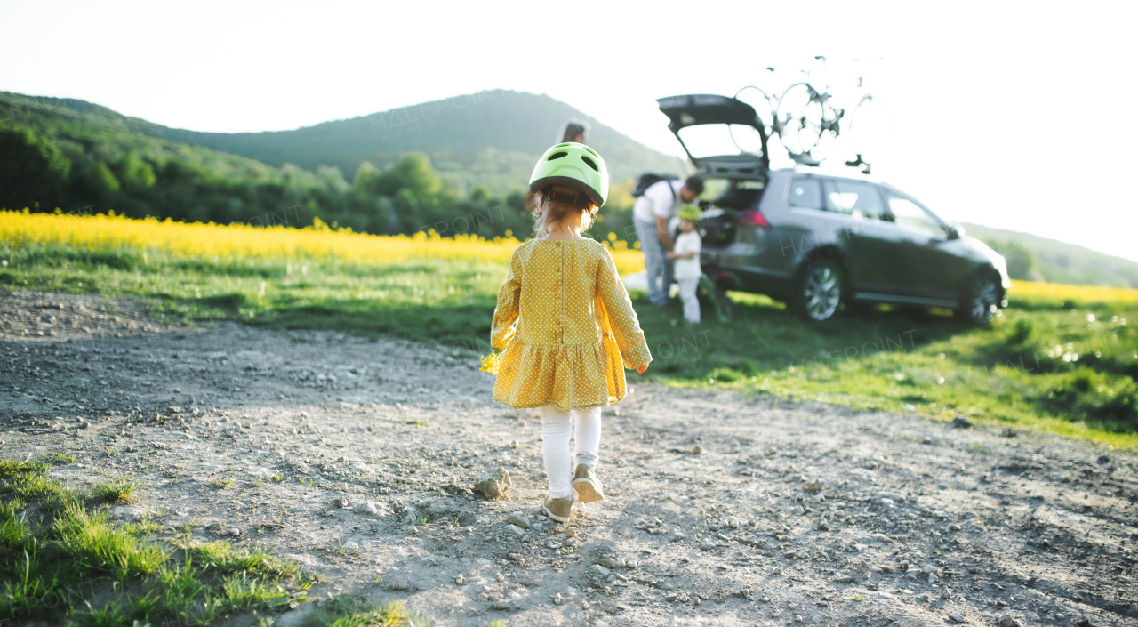 Rear view os small girl with family going on cycling trip in countryside, walking.