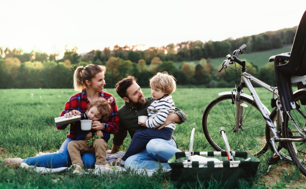 Front view of family with two small children on cycling trip, sitting on grass and resting.