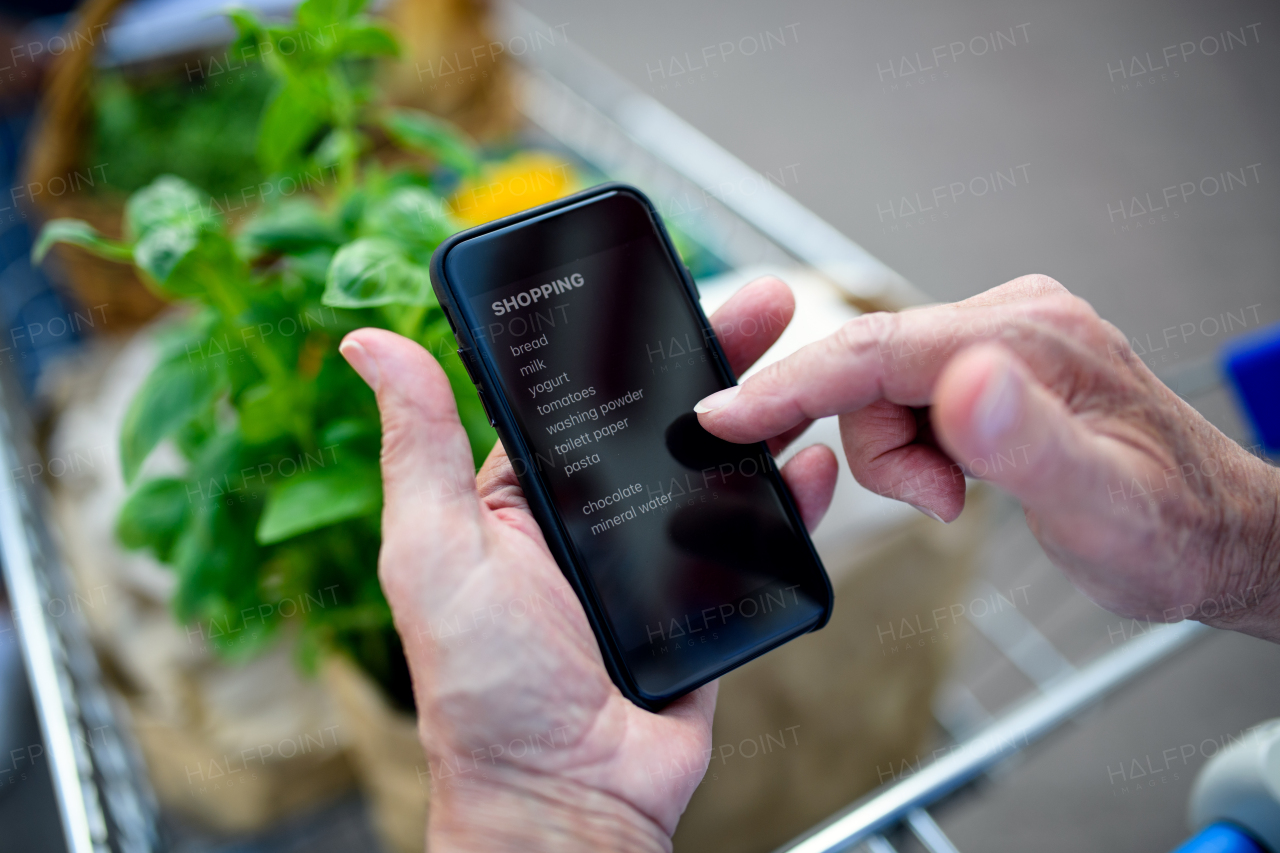 Unrecognizable senior couple man with smartphone list doing shopping in supermarket.