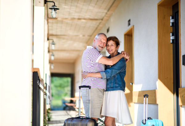 Senior couple with luggage hugging outside apartment on holiday, back to normal concept.