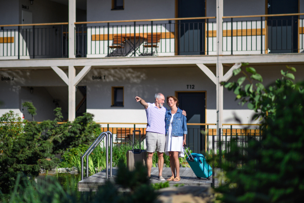 Senior couple with luggage outside apartment on holiday, back to normal concept.