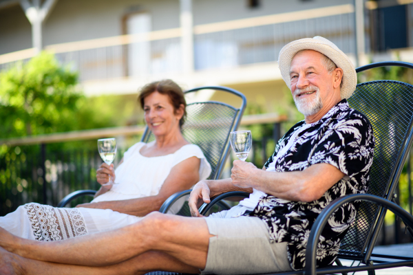 A senior couple holding wine outdoors on holiday, relaxing.