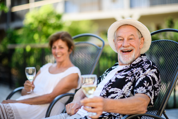 A senior couple holding wine outdoors on holiday, looking at camera.