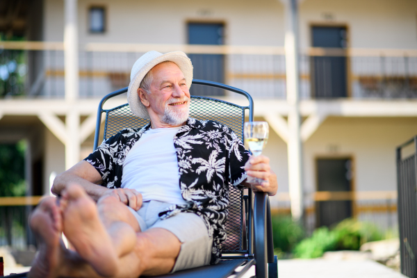 Portrait of senior man holding wine outdoors on holiday, relaxing.