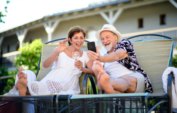 Cheerful senior couple with smartphone outdoors on holiday, video call concept.